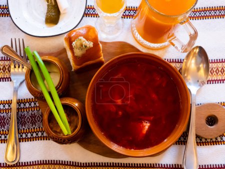 Clay bowl of thick red borscht garnished with pampushky, minced salo, garlic, greens and smetana. Main dish of Ukrainian cuisine