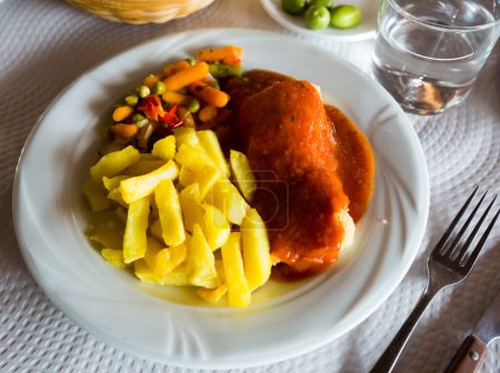 Delicious baked codfish fillet with tomato sauce and side dish of fried potatoes and vegetable salad