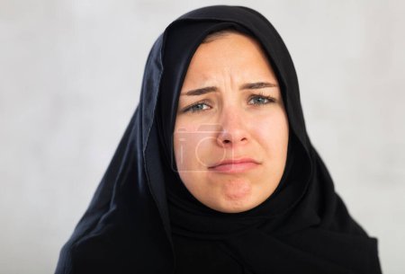 joven mujer musulmana en el hiyab negro está molesto por las malas noticias y abatida sostiene sus manos palmas hacia arriba.Mujer frustrada en dupatta está gesticulando activamente y sacudiendo sus manos.Primer plano sobre fondo gris