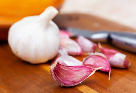 Cutting board with fresh seasonings on a wooden background. White garlic heads. Condiments