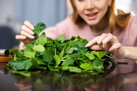 Happy girl carefully examines spinach leaves for salad