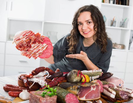 Happy woman costs near table on which sausages and smoked meat lie