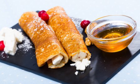 Bulgarian-style crepes Palatschinke with filling of soft cheese and walnuts with honey on black board