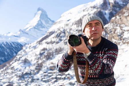 Traveler with passion for photography enjoying hiking in Swiss Alps in wintertime, taking pictures of nature with professional camera
