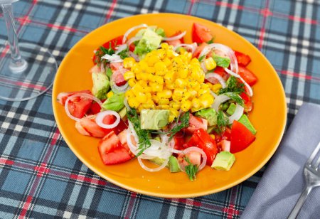 Delicious light vegetable salad made from tomatoes, canned corn, avocado and onion sliced into rings