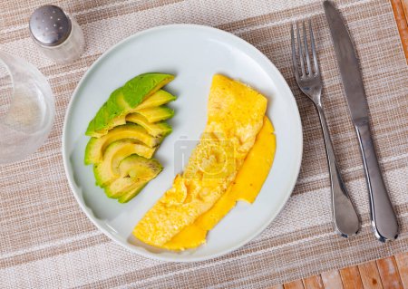 Light and hearty breakfast is served in restaurant - delicate omelette and half avocado fruit, cut into slices
