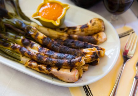 National Catalan winter dish. Delicate grilled calcots traditionally served with romesco sauce and red wine in restaurant..