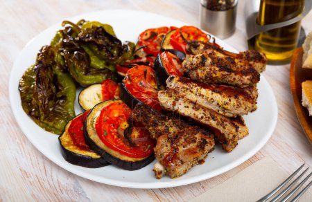 Grilled pork ribs rack garnished on white plate with eggplant, tomatoes and bell pepper. High quality photo