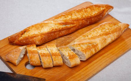 Closeup of long thin French loaves with chopped slices on wooden surface. Fresh baked goods