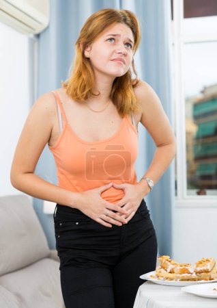 Young woman is having a stomach ache after overeating at home.