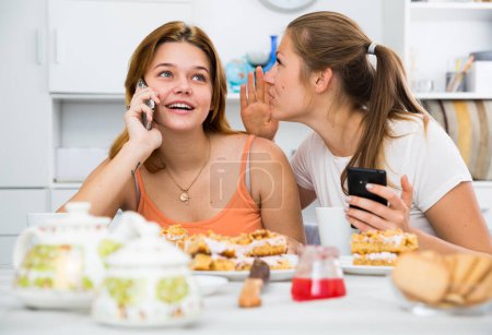 Girlfriends are playfull talking by phone at home.