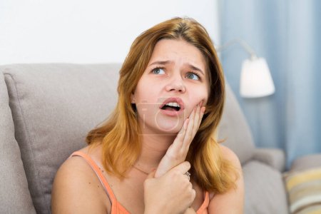 Triste joven mujer en el sofá cogida de la mano en el diente de la enfermedad