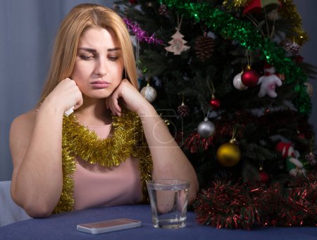 Traurige Frau langweilt sich in der Silvesternacht zu Hause mit einem Glas Wasser.