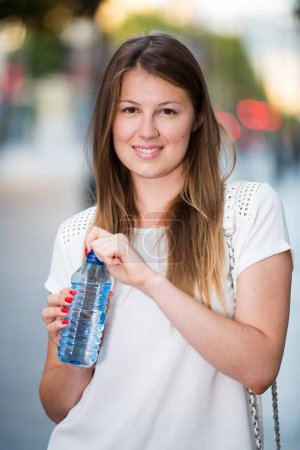 Attractive girl drinking water during walk around city in hot summer day