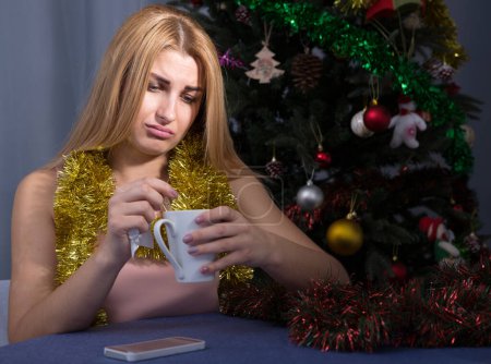 Junge Frau trinkt Tee und langweilt sich allein in der Silvesternacht zu Hause.