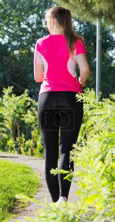 Female 20-30 years old is jogging back in pink T-shirt in the park.