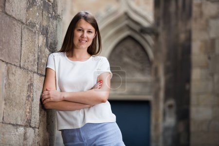 Glückliche junge Frau schlendert durch die Stadt und steht an alter Steinmauer