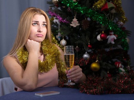Junge Frau trinkt Champagner und langweilt sich allein in der Silvesternacht zu Hause.