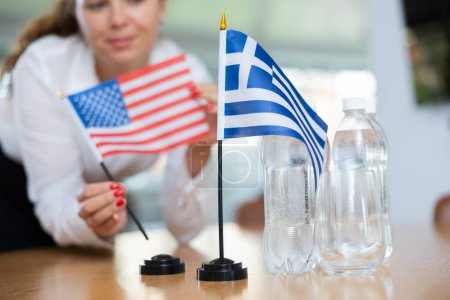 Asistente joven que establece banderas griegas y americanas para las negociaciones internacionales