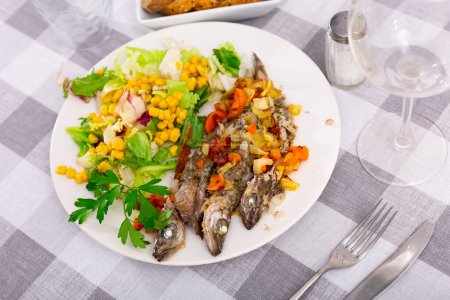 Appetizing fried blue whiting with vegetables, served with a light salad of canned corn, Peking cabbage and lettuce leaves