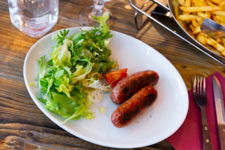 Beliebtes Gericht der europäischen Küche ist die Savoyer Wurst, serviert mit einer Scheibe geschnittener Tomaten und Salat