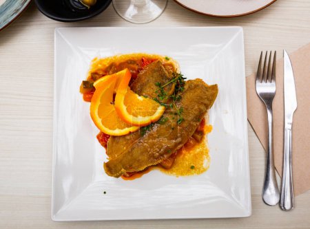 Delicious black sole fish served with stewed vegetables and fresh orange garnished with greens