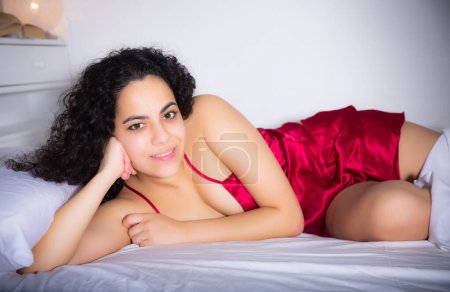 Attraktive junge Mädchen in roten Dessous posieren auf dem Bett