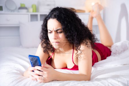 Sexy junges Mädchen in roten Dessous mit Handy auf dem Bett