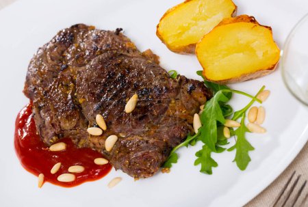 Delicious well done fried beef loin served with vegetable garnish of baked potato, tomato sauce and pine nuts