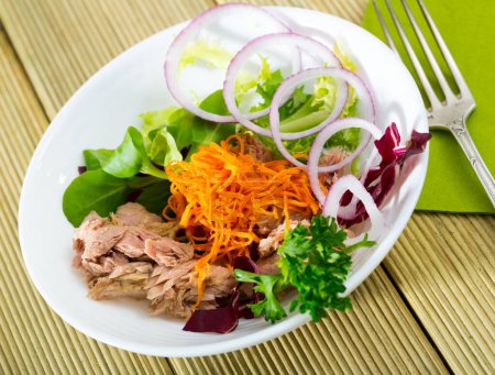 Tasty salad of grated carrots with canned tuna, sliced red onion and fresh greens..