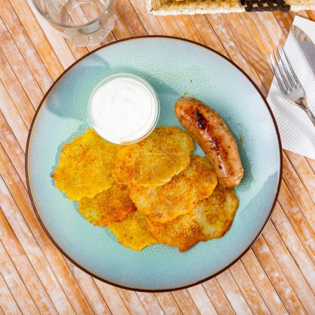 Potato fritters garnished with yogurt sauce and grilled sausage