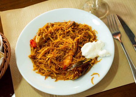 Delicious traditional Valencian seafood fideua, savory pasta dish with shrimps, squid and clams served on plate with sauce allioli