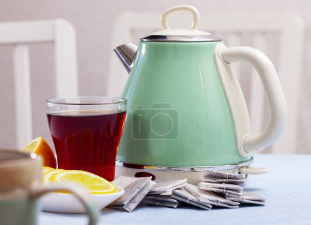 Two cups with fresh black tea on wooden table with vintage light green electric kettle and slices of lemon on plate..
