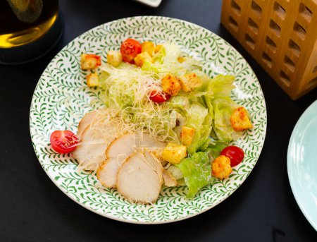 Caesar salad with chicken served on circular plate in restaurant.