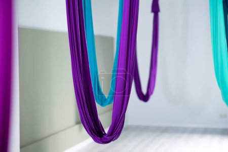 View of multicolored suspended silk hammocks for aerial or anti-gravity yoga in empty modern fitness studio. Popular leisure, recreation, sports activity and wellness concept..