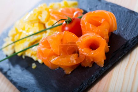 Omelet with salmon garnished with fresh scallion and cherry tomato on black serving board..