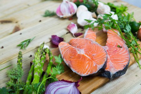 Delicious salmon steaks with fresh vegetables and mushrooms on wooden background