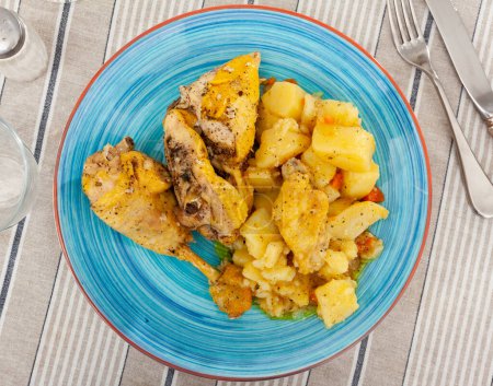 Tasty baked chicken drumsticks and potatoes at plate closeup
