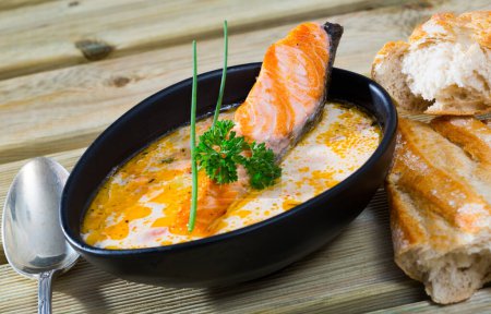 Delicious creamy salmon soup in black bowl served with baguette