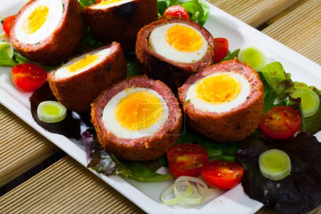 Traditional Scottish dish - halved Scotch eggs with garnish of vegetables and greens on white serving plate
