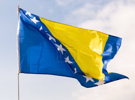 Bandera de Bosnia y Herzegovina ondeando sobre un cielo azul
