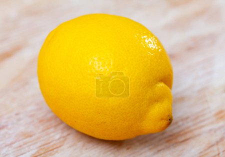 There is whole yellow lemon on wooden table. Lemon peel texture close-up, isolated