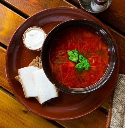 Ukrainian borsch red soup with pork and sour cream , served with bread and salo
