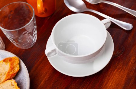 Des plats sont préparés pour les repas sur une table en bois. Il y a une assiette de soupe profonde dans le dîner blanc, et les couverts sont disposés à côté de lui