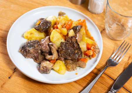 Auf dem Tisch steht ein deftiges Mittagessen - Kalbfleisch mit geschmortem Gemüse. Champignons, Kartoffeln, Erbsen mit großen Rinderfiletstücken gekocht.