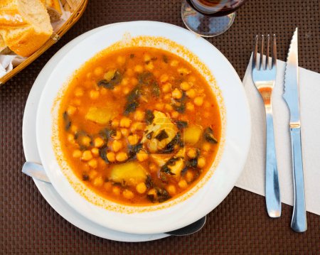 Hearty Mediterranean lunch is cooked on plate - soup stew boiled of cod fillet, potatoes, chickpeas in tomato sauce.