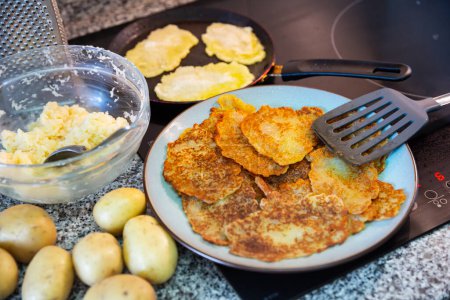 Potato fritters in frying pan and ingredients on table, home cooking