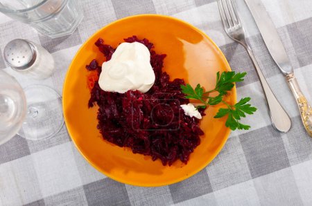 Portion of salad made of boiled and grated beetroot served on table with sour cream.