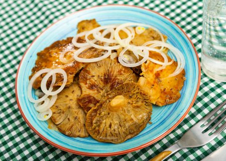 Appetizing juicy pickled russula delica, sprinkled on top of onion rings on a plate