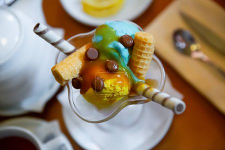Balls of yellow and blue ice cream with waffle tube in glass ramekin on table. Top view